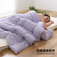 淺紫色舒芙蕾透氣四季被，中棉款，觸感蓬鬆柔軟，表面有細緻的紋理，覆蓋在一位女性身上，她正安詳地睡在床墊上，背景為木地板與植物。