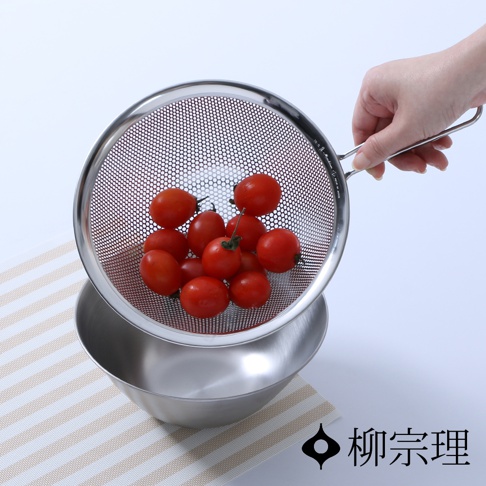 不鏽鋼單柄漏杓，網孔細密，裝有新鮮小番茄，置於同材質的碗上方，背景為淺色調。