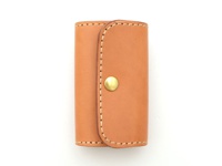 淺棕色皮革製作的六鉤鑰匙包，採用經典的閉合設計，配有金色金屬按扣，車縫線清晰，展現職人手作質感。