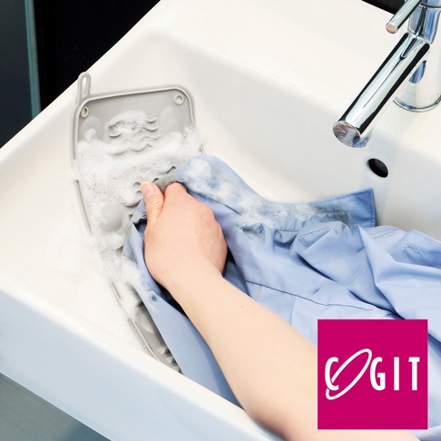 COGIT 品牌標誌旁的藍色襯衫正在一個帶有泡沫的白色水槽中被清洗，手部也浸在水中。