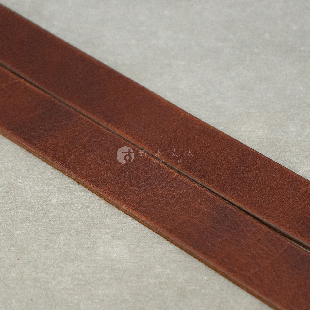 精緻的深棕色皮革皮帶，帶有細膩的紋理，呈現職人手作的質感，圖片右側可見「SUZUKI SHOP」的品牌標誌