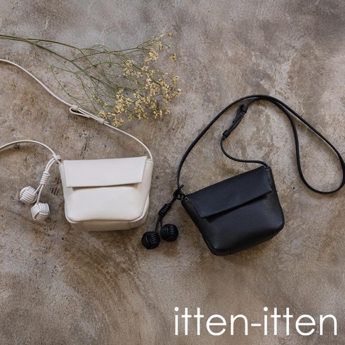 itten-itten 品牌的白色和黑色義大利皮革迷你單肩包，配有獨特的點結吊飾，在粗糙的灰色背景上展示。