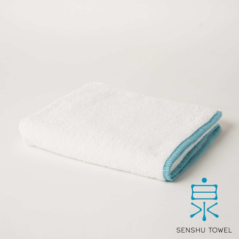 白色長纖毛巾，邊緣滾有藍色滾邊，質地蓬鬆柔軟，帶有緞澤光澤。