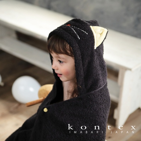 一對可愛的黃色條紋貓耳朵點綴在黑色連帽浴巾的頂部，浴巾由柔軟的今治純棉製成，由一個小女孩穿著。