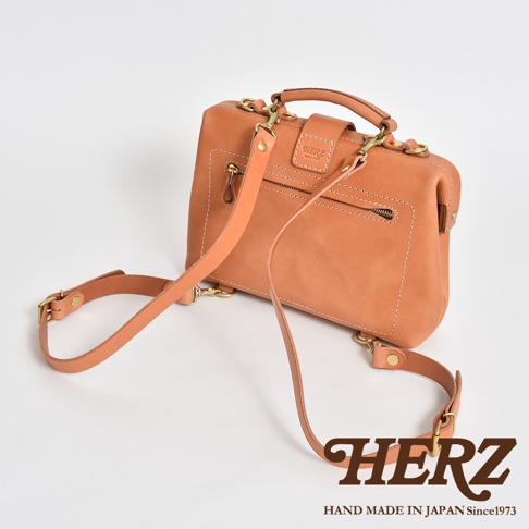 皮革迷你軟皮杜勒斯包，淺棕色，配有可拆卸肩帶和金色金屬配件，正面有一個拉鍊口袋和品牌標誌。