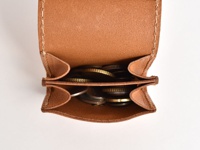 職人手作皮革雙折收納零錢包，呈現自然棕色皮革，內部裝有各式硬幣。包體結構清晰，縫線精緻，展現皮革的質感與實用性。