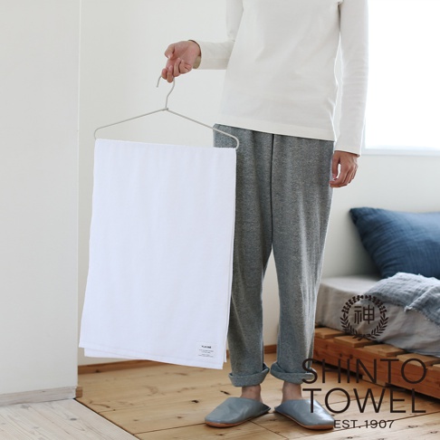 一條白色蓬鬆的迷你浴巾，材質為有機棉，掛在衣架上，由一位穿著灰色長褲和白色上衣的人士展示。