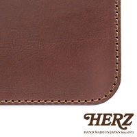 HERZ 品牌標誌，下方為 HAND MADE IN JAPAN Since1973 字樣，搭配部分深棕色皮革的特寫，顯示出皮革的紋理及縫線細節。