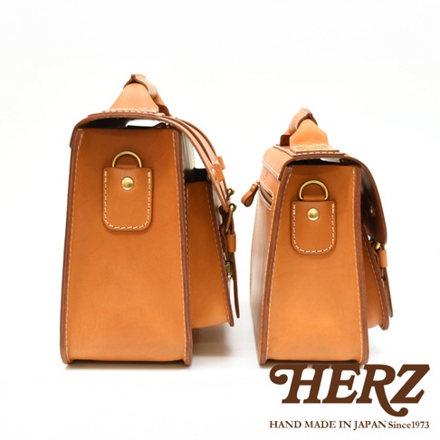 兩個職人手作皮革經典雙扣兩用單肩包，皆為棕褐色，採用厚實皮革製成，側面有雙扣設計和金屬釦環，其中一個包的頂部有提把，另一個包的側邊有拉鍊。