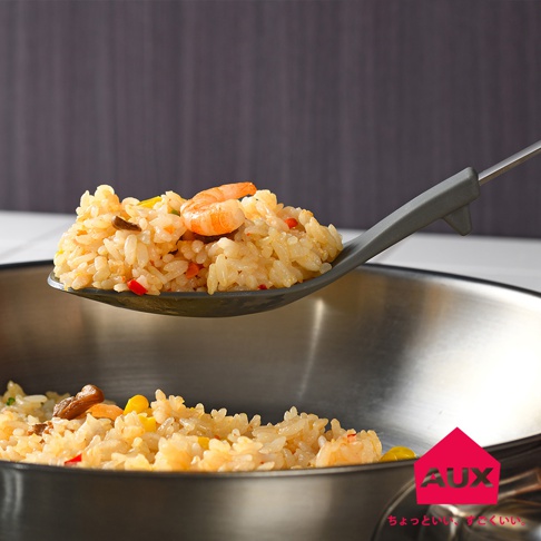 灰色不沾桌拌炒量匙盛著炒飯，飯中含有蝦仁、玉米粒、紅椒丁及其他配料，下方是炒鍋裡的炒飯。