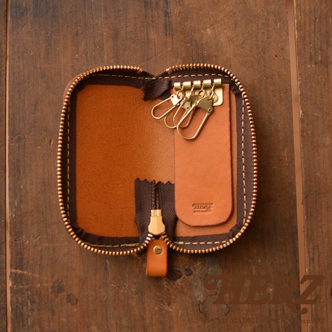 一個棕色皮革製成的鑰匙包，打開狀態，露出內部四個金屬掛鉤和皮革拉鍊。