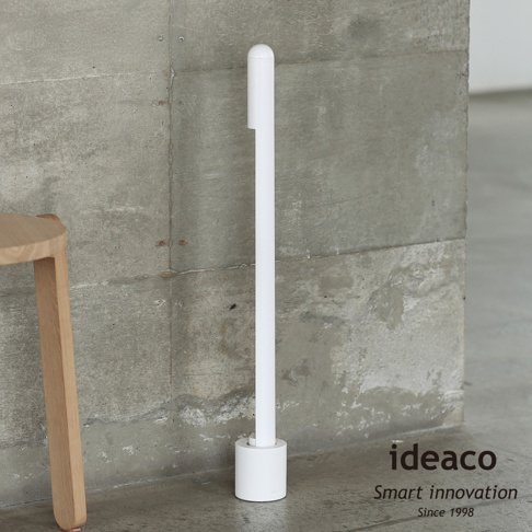 ideaco 附收納座的白色長柄鞋拔，立於灰色水泥牆前