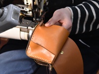 職人手作的皮革中型雙折短夾，以淺棕色皮革製成，車縫著米白色線跡，並有一個金屬按扣。