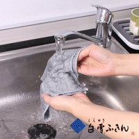 一雙手正在水龍頭下沖洗一條灰色網狀織物的家事拭巾，拭巾邊緣有白色滾邊。