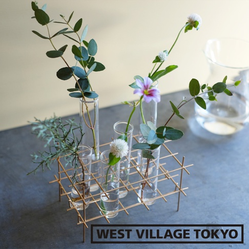 金屬網架上放置著多個玻璃試管花器，內插有綠葉枝條、紫色小花及白色球狀花朵，整體呈現簡約自然風格。