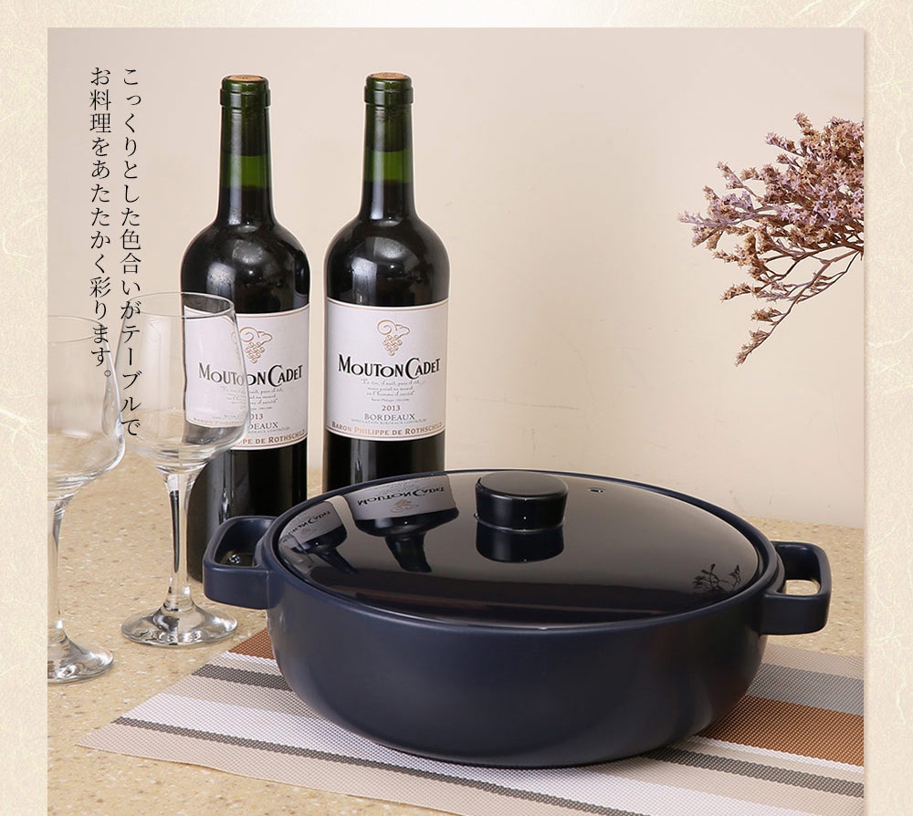 海軍藍色陶土湯鍋，配有黑色鍋蓋和把手，擺放在桌面上，旁邊有兩瓶紅酒和兩個高腳杯。