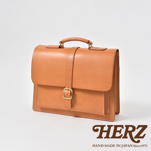 一個 tan 色皮革手提包，配有單扣和皮帶封口，以及頂部提把。