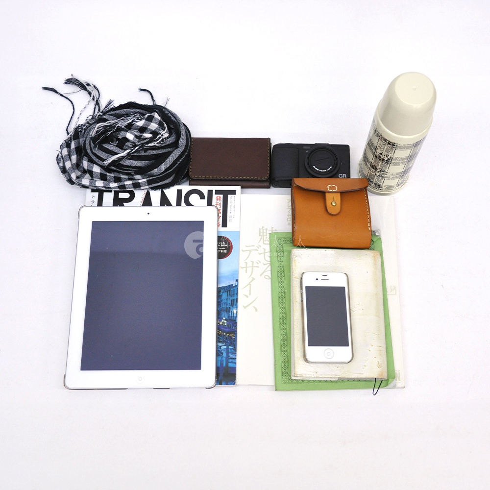 職人手作皮革多口袋後背包 R-135 (共5色) 的圖片展示了背包內的物品：白色平板電腦、黑色相機、棕色皮夾、棕色小皮包、黑白格紋圍巾、印有日文雜誌、綠色筆記本和白色手機，以及一個格紋保溫瓶。