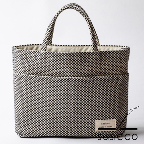 三河木綿刺子織多口袋托特包，黑色與米色格紋圖案，織紋清晰，包體寬敞，外部設有兩個大口袋，手把為圓筒狀，內襯為米色棉布，整體造型簡潔實用。