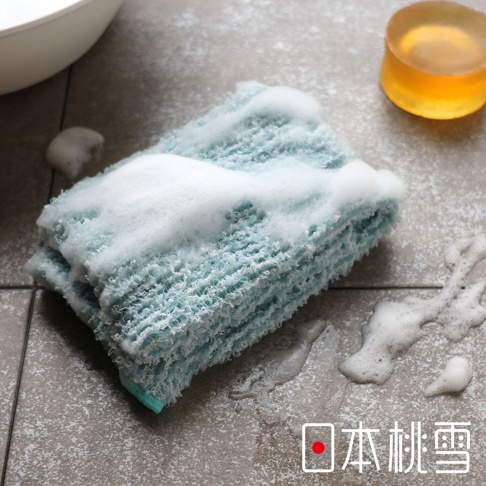 日本桃雪品牌的沐浴巾，上面覆蓋著豐富的白色泡沫，旁邊有一塊圓形的黃色肥皂。