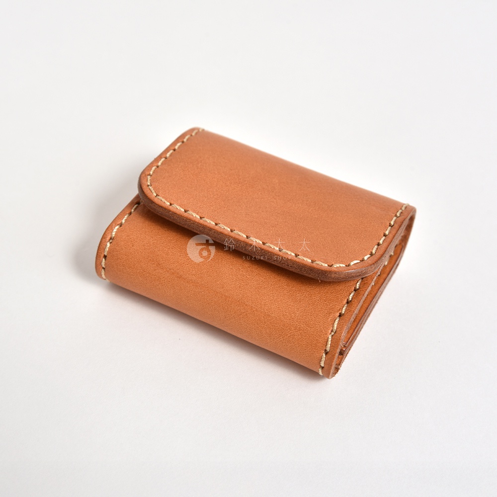 一個由日本品牌HERZ職人手工製作的棕色皮革雙折零錢包，呈現簡約的長方形外觀，採用高品質Stare皮革材質，邊緣以淺色縫線加固，展現出質感細膩的職人手作風格，整體設計小巧俐落。