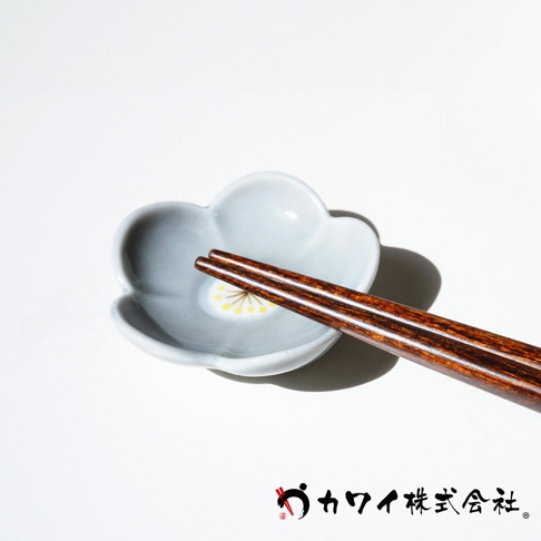 一雙深棕色木質筷子放置在淺灰色梅花形陶瓷筷架上，筷架中央飾有黃色花蕊圖案。