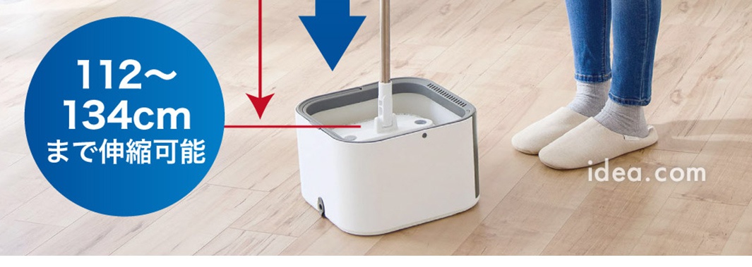 一個正在進行清潔作業的旋轉拖把，桶身為白色搭配灰色邊框，拖把桿垂直插入桶中，圖片左側標示該拖把長度可在112至134公分之間伸縮調整，旁邊有一名穿著藍色牛仔褲與室內拖鞋的人站立，呈現家居清潔場景。