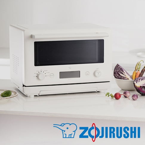 白色象印烘烤微波爐 ES-JAF23，配有黑色網狀烤箱門、數位顯示螢幕、多個控制旋鈕和按鈕。爐體側面有散熱孔，前方底部有下拉式烤盤。烤箱旁擺放著一碗切塊的紫甘藍、胡蘿蔔、小蘿蔔等新鮮蔬菜。