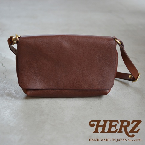 HERZ 品牌標誌，下方印有 HAND MADE IN JAPAN Since1973 字樣，旁邊有一個棕色皮革製成的隨身斜背包。