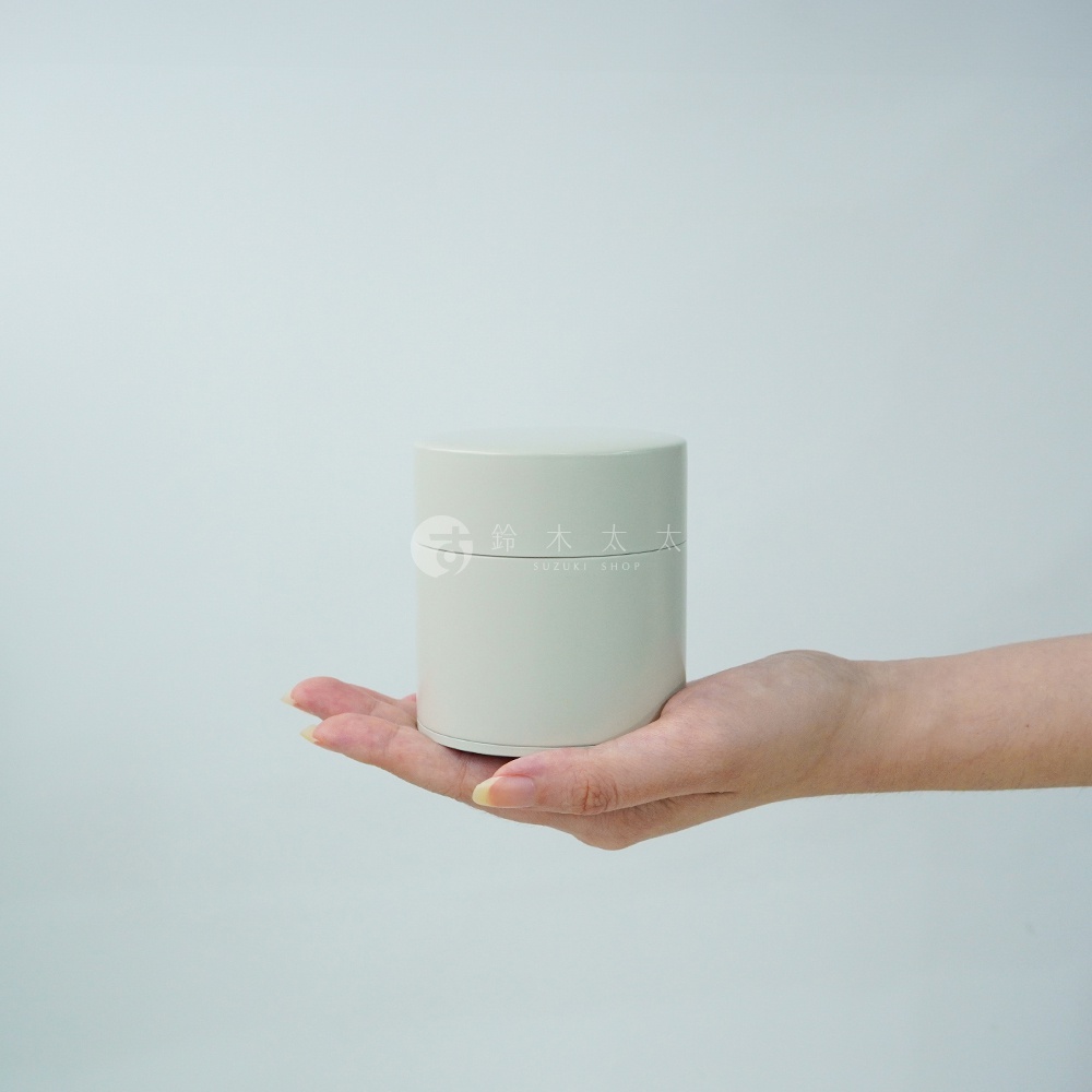 一隻手捧著一個簡約淺灰色圓柱形錫製茶葉罐，罐身上有「鈴木太太 SUZUKI SHOP」的標誌。
