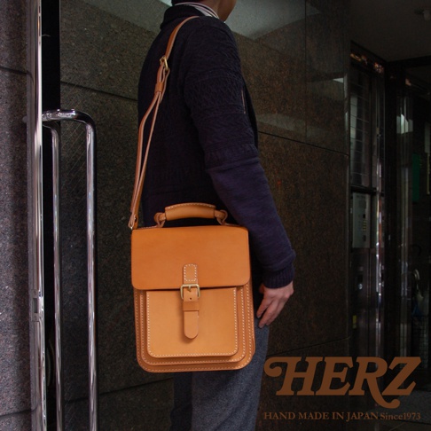 職人手作皮革單肩兩用小方包，天然棕色皮革，帶有金色釦環和縫線細節，可肩背或手提。
