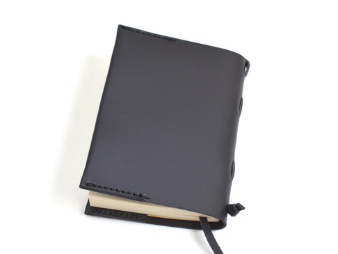 黑色皮革書套，附有縫線裝飾及綁帶，套著一本淺色封面的書籍。