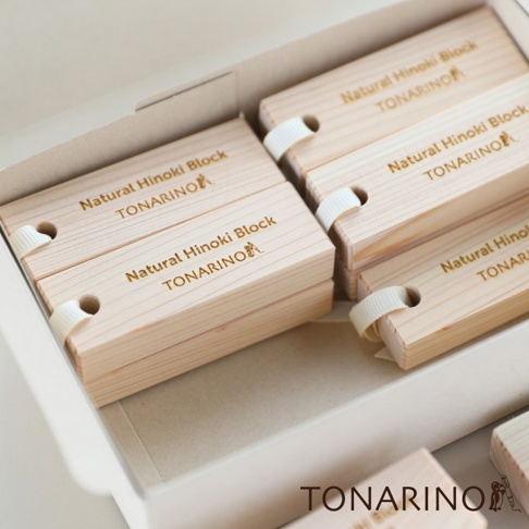 一盒裝有16個淺色天然檜木條，每個檜木條上都印有金色字體「Natural Hinoki Block TONARINO」及圖案，並以白色緞帶繫住。