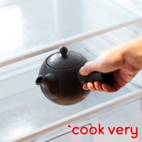 一只手正在將一個黑色的、帶有圓形壺蓋和短嘴的常滑燒咖啡急須茶壺放入一個透明的冰箱架中。