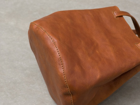 職人手作皮革Organ抽繩肩背手提托特包，M尺寸，呈現溫潤的焦糖棕色皮革，包身線條柔和，帶有自然的皮革紋理和手工縫線細節，展現質感。