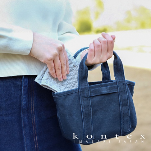 一名女士手持深藍色帆布托特包，包內裝有一塊淺灰色、帶有鬆餅紋理的棉麻混紡方巾。