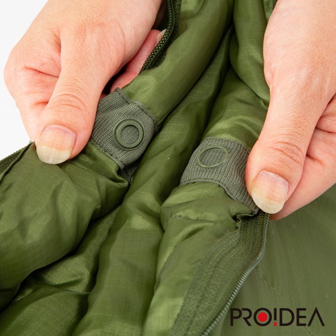 雙手正在操作一個軍綠色、尼龍材質的兩用睡袋，展示其內部的按扣和拉鍊設計。