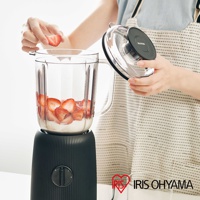 黑色條紋果汁機，附透明玻璃杯，杯內有牛奶和切片草莓。一人手持透明杯蓋，正準備蓋上。