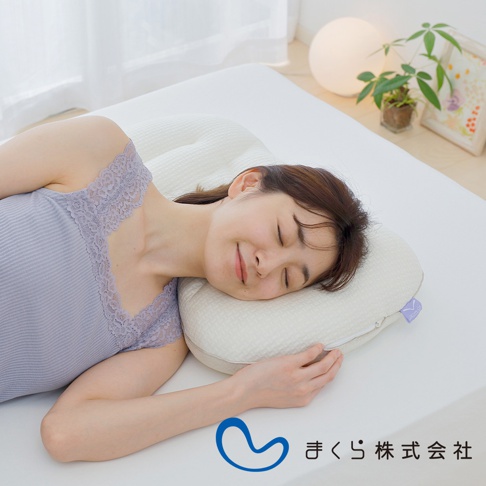 一位女性仰躺於白色床墊上，臉部朝右，頭部倚靠在一個米白色、紋理細緻的枕頭上。枕頭呈現圓潤的弧形，表面有蜂巢狀的紋路，一側有紫色品牌標籤。