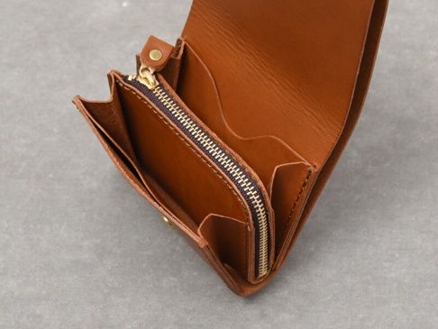 職人手作皮革Organ雙折迷你短夾，採用棕色鞣製皮革製成，展現自然紋理。內部設有拉鍊零錢袋及多個卡槽，金色拉鍊與銅製按扣增添質感。