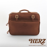 棕色皮革製成的雙用商務公事包，採用兩條拉鍊開口、頂部提把，並配有兩個金色搭扣裝飾。包包正面中央有一個橢圓形壓印品牌標誌。