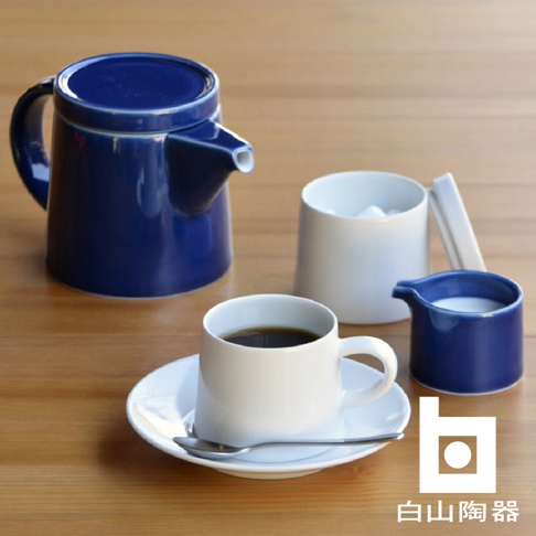 藍色M型壺，白色咖啡杯與盤子，白色糖罐，藍色奶盅，以及銀色湯匙，皆為陶瓷材質，置於木質桌面。