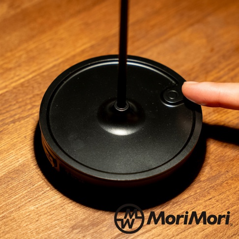 黑色金屬復古氛圍燈底座，帶有按鈕，手指正按下開關，置於木質桌面。