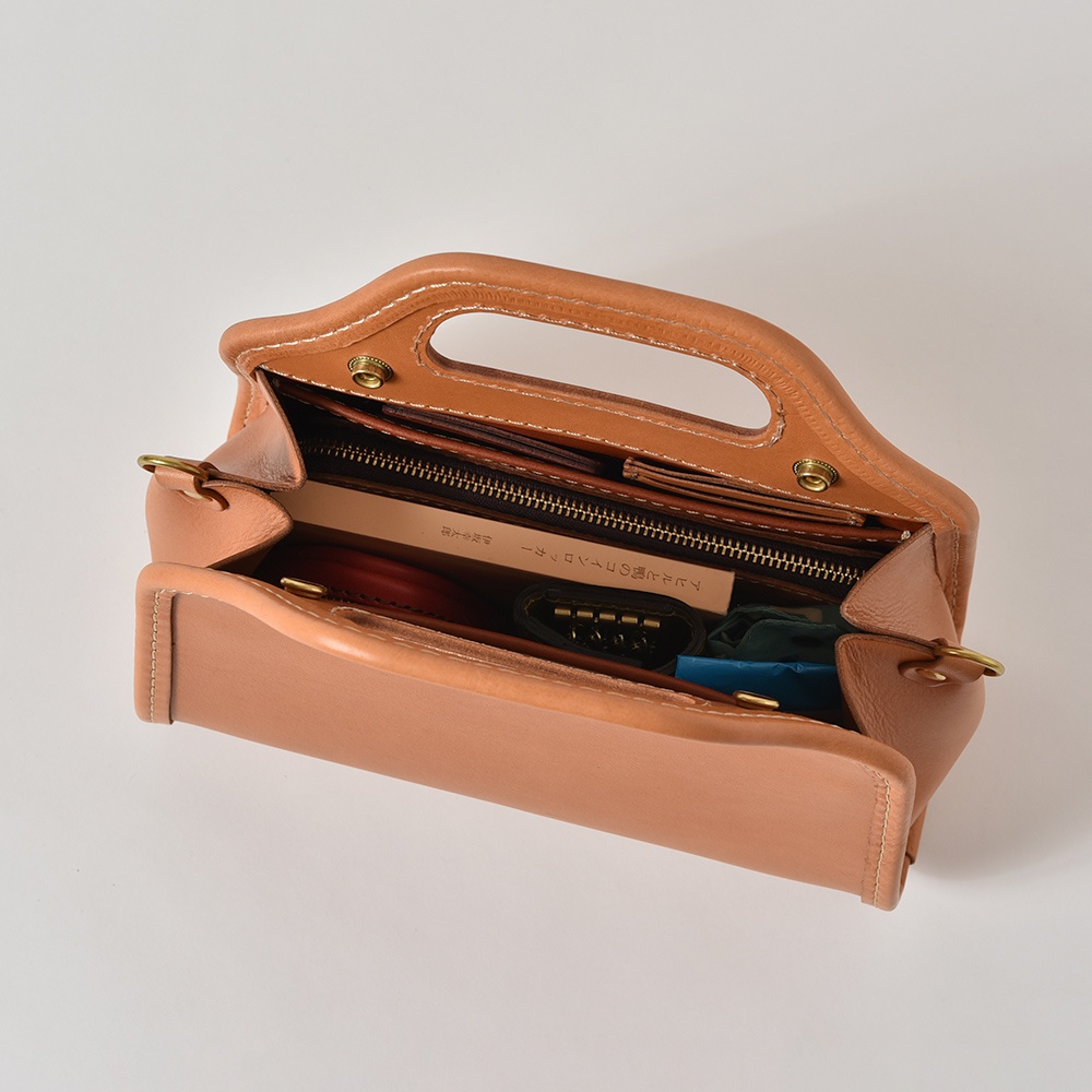 淺棕色皮革製成的職人手作單肩兩用拱型手袋，內有拉鍊隔層，可見鑰匙包、卡夾等物品。