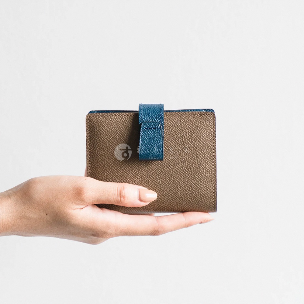 Atelier nuu noble皮革雙折短夾，棕色皮革搭配藍色封口帶，由手托起
