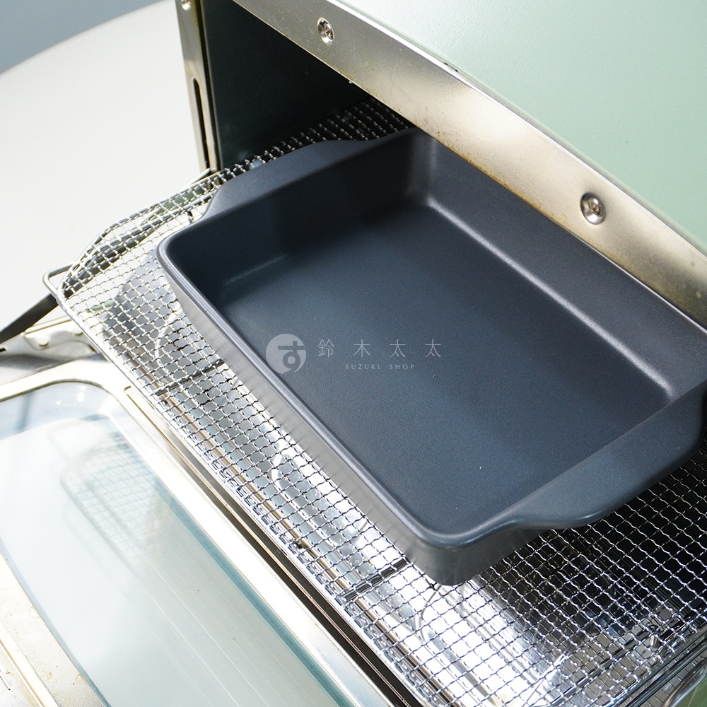 深灰色耐熱陶製萬用長方形烤盤，平底設計，放置於烤箱的鐵網架上。