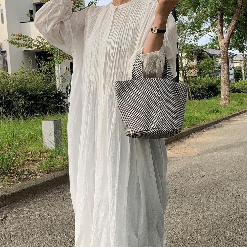 一位女性手持黑色與白色格紋圖案的圓底水桶包，包款材質為刺子織。