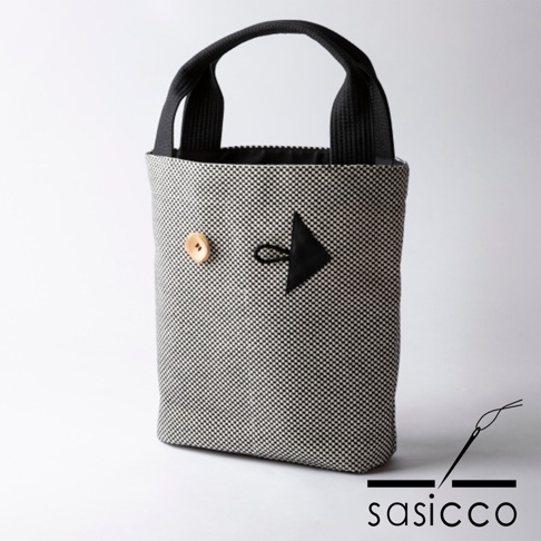 三河木綿刺子織直式收納托特包，以黑白格紋布料製成，配有黑色提把。包身正面裝飾有木質鈕扣和一個黑色箭頭形狀的皮革裝飾，箭頭下方有一圈黑色縫線。