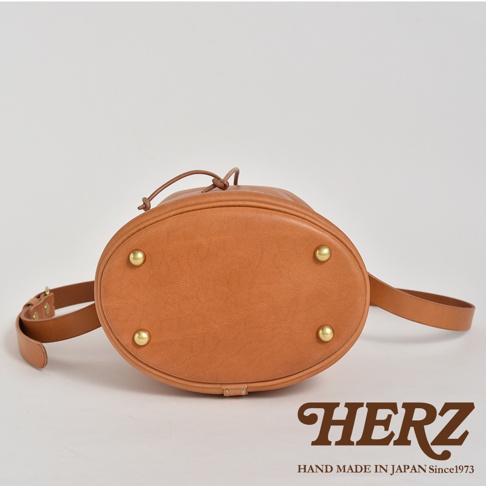 棕色皮革束口單肩包，底部有四個黃銅鉚釘，附有可調節的皮革肩帶。