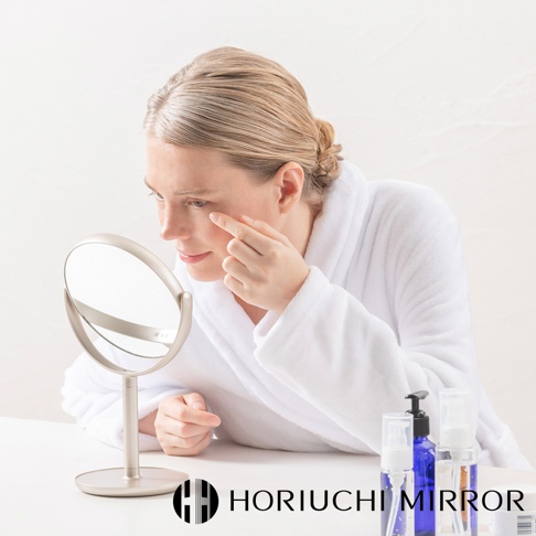 NAPURE 香檳金桌上型化妝圓鏡，鏡面呈現，金屬支架與底座，周圍有化妝品瓶。